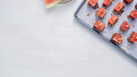 Dipping watermelon cubes into melted chocolate and garnishing with sea salt and almonds.