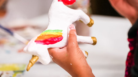Little girls painting paper mache unicorn with acrylic paint.