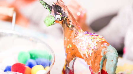 Little girls decorating paper mache unicorn with glitter and paper flowers.の写真素材
