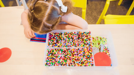 Little girl making bracelet from colorful kids beads.