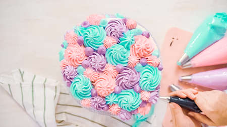 Flat lay. Piping pastel color buttercream rosettes on a white cake to make a unicorn cake.の写真素材