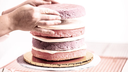 Baker assembling pink and purple cake layer to make unicorn cake for little girl's birthday party.