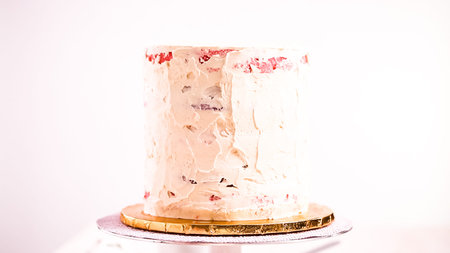 Baker frosting pink and purple cake with a white buttercream icing.