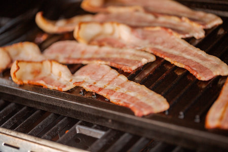 Grilling bacon strips on cast iron griddle in outdoor gas grill.の写真素材