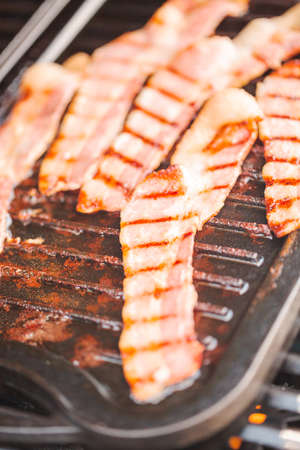 Grilling bacon strips on cast iron griddle in outdoor gas grill.の写真素材