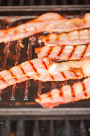 Grilling bacon strips on cast iron griddle in outdoor gas grill.の写真素材