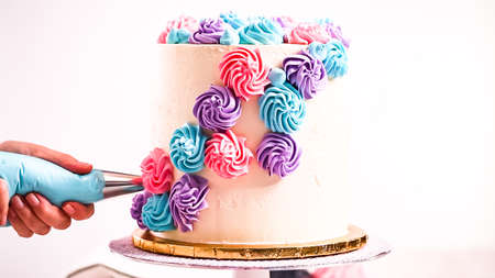 Baker piping pastel color buttercream rosettes on a white cake to make a unicorn cake.の写真素材