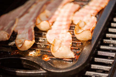 Grilling bacon strips on cast iron griddle in outdoor gas grill.の写真素材