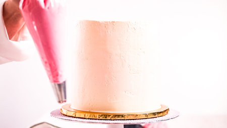 Baker piping pastel color buttercream rosettes on a white cake to make a unicorn cake.の写真素材