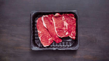 Raw New York strip steaks in black plastic meat packaging container.の写真素材