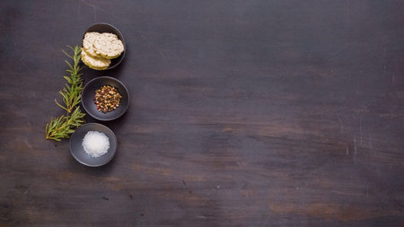 Salt, peppercorns and herb butter in small containers on blacvk wood table.