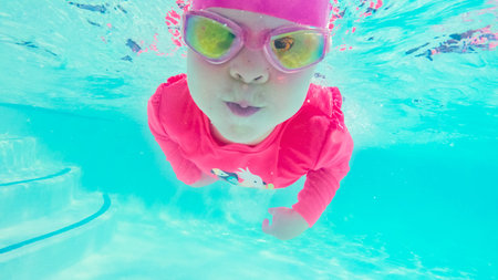 Little girl having fun swimming under the water in outdoor pool.