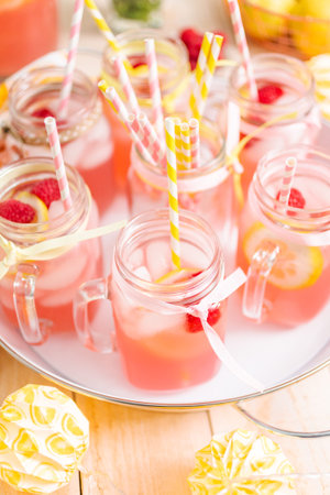 Raspberry lemonade garnished with fresh lemon and raspberries in drinking mason jars.