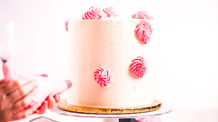 Baker piping pastel color buttercream rosettes on a white cake to make a unicorn cake.