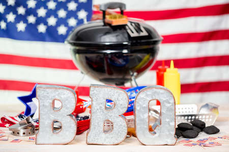 Metal BBQ sign on small round charcoal grill with July 4th decorations.の写真素材