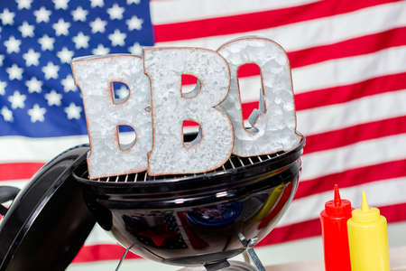 Metal BBQ sign on small round charcoal grill with July 4th decorations.の写真素材