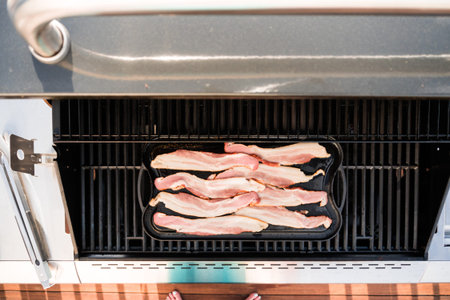 Frying bacon on cast iron griddle in outdoor gas grill.の写真素材