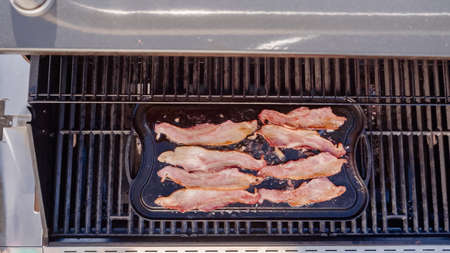 Frying bacon on cast iron griddle in outdoor gas grill.の写真素材