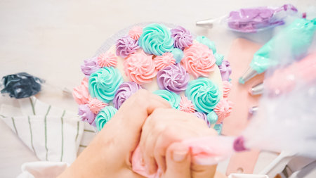 Flat lay. Piping pastel color buttercream rosettes on a white cake to make a unicorn cake.の写真素材