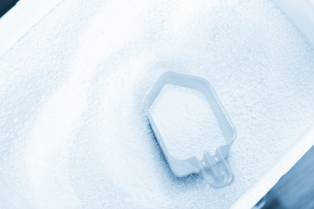 Pink plastic laundry detergent measuring cup in white laundry detergent bucket.