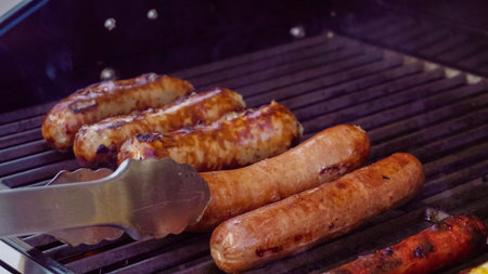 Cooking hot dogs and bratwurst on outdoor gas grill in the Summer.
