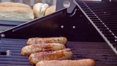 Cooking hot dogs and bratwurst on outdoor gas grill in the Summer.