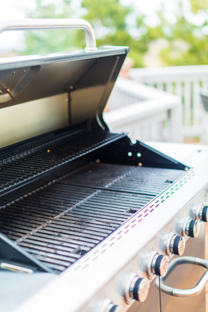 Six burner outdoor gas grill with open lid on backyard.