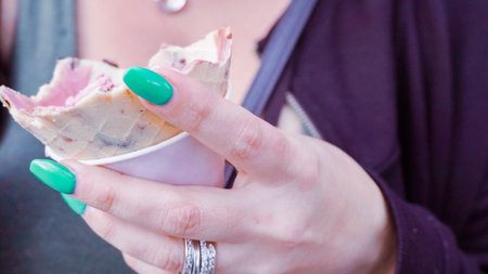 Moman with blue nails eating ice cream outside.
