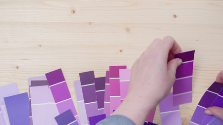 Variety of paint swatches with shades of purple pain on unfinished wooden background.