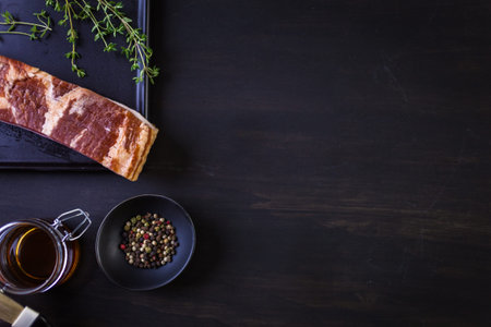 Raw bacon strips with fresh spices on a black ccutting board.の写真素材