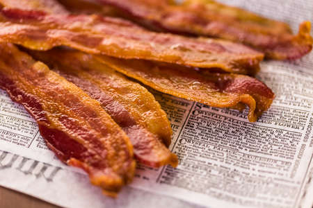Cooked bacon strips on a newspaper.の写真素材