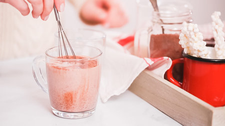 Mixing hot chocolate mix in glass cup with with small whisk.