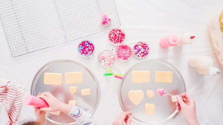Flat lay. Step by step. Little girl decarting sugar cookies with royal icing and sprinkles for Valentine's Day.の写真素材