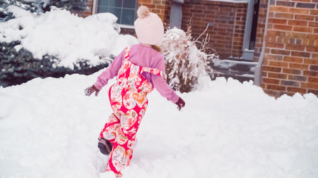 Little girl playing in snow near her house in typical suburbia.