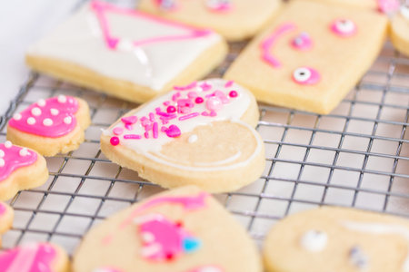 Decorating heart shape sugar cookies with royal icing and pink sprinkles for Valentine's day.