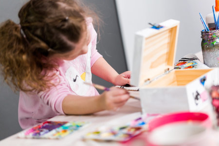 Little girl painting a unicorn on a wood box with acrylic paint.