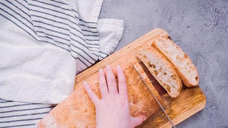 Photo pour Flat lay. Slicing fresh ciabatta bread on a wood cutting board. - image libre de droit