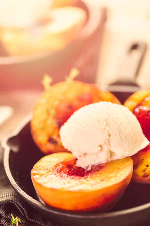 Organic grilled peaches with scoop of vanilla ice cream on a cast iron frying pan.の写真素材
