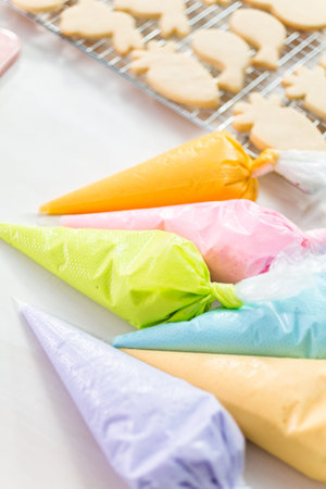 Piping bags with pastel color royal icing to decorate Easter sugar cookies.