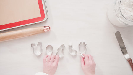 Step by step. Flat lay. Cutting sugar cookie dough with Easter shaped cookie cutters.
