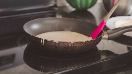 Cooking Russian pancake in old frying pan on top of electric stove.