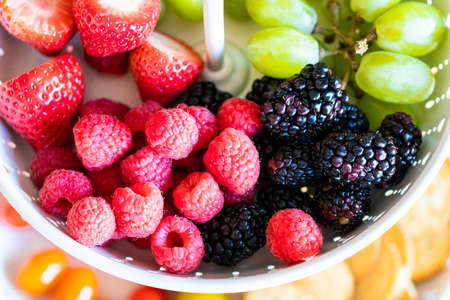 A white tiered platter filled with smoked salmon, cheese, crackers, and fresh fruits and berries.の写真素材
