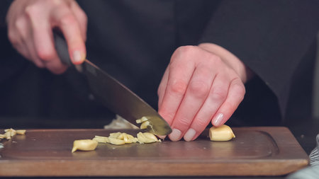 Step by step. Dicing organic garlic on wood cutting board.
