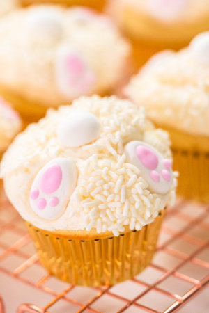 Decorating vanilla cupcakes with a white buttercream icing and bunny ears for Easter.