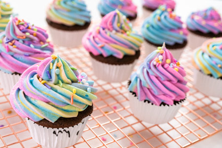 Decorating chocolate unicorn cupcakes with colorful buttercream icing and sprinkles.の写真素材