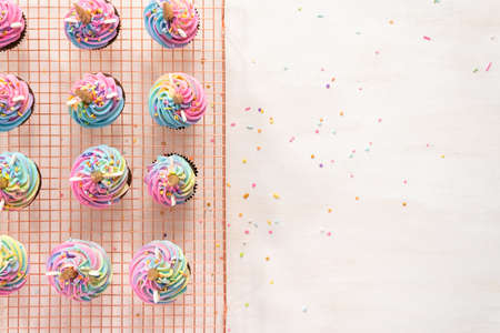 Flat lay. Decorating chocolate unicorn cupcakes with colorful buttercream icing and sprinkles.の写真素材