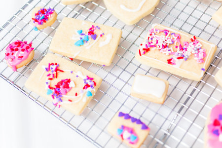 Decorating heart shape sugar cookies with royal icing and pink sprinkles for Valentine's day.