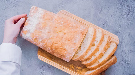 Flat lay. Slicing fresh ciabatta bread on a wood cutting board.