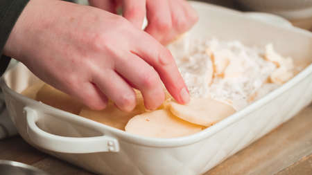 Preparing scalloped potatoes in a white ceramic baking dish.の写真素材