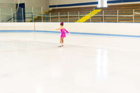 Little figure skater in pink dress practicing on the indoor ice rink.の写真素材